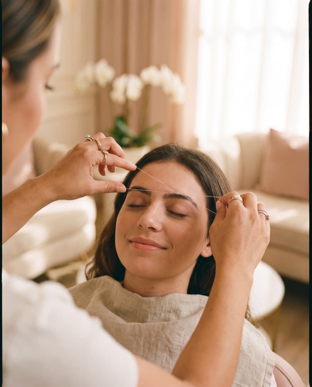 An esthetician performing precise eyebrow threading — the craft that built our name